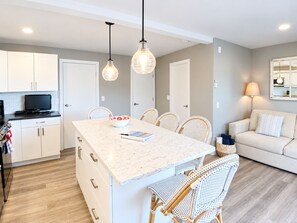 A modern kitchen with white cabinets, a marble island, and a dining area with wicker chairs.