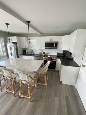 A modern kitchen with white cabinetry, a marble island, wicker chairs, and stainless steel appliances.