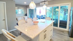 A kitchen with a marble countertop, white cabinetry, wicker chairs, and pendant lighting.