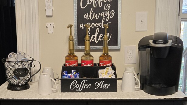 A coffee bar with a sign reading "Coffee Bar" and a chalkboard sign above stating "Coffee is always a good idea." There are three bottles of Trani coffee, a coffee maker, and a coffee pot on the counter. - Charming 2-bedroom house in close proximity to the YUM Ctr, the Downs, etc. (Louisville)