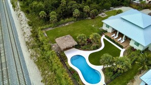An aerial view of a property with a swimming pool, a thatched-roof structure, and a house with a blue roof.