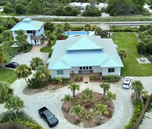 A large house with a blue roof, surrounded by a well-maintained lawn and palm trees. - Indian River Retreat  - Main House and Cottage (Jensen Beach)