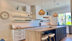 A modern kitchen with white cabinetry, a wooden island, pendant lights, and a view of greenery outside.