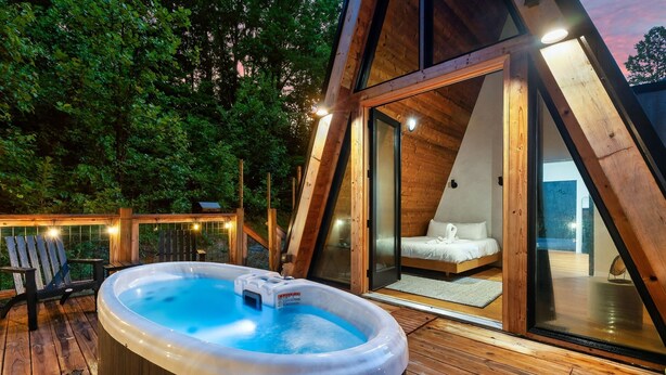 Una terraza de madera con un jacuzzi, una cama y una puerta de vidrio que da a un dormitorio.