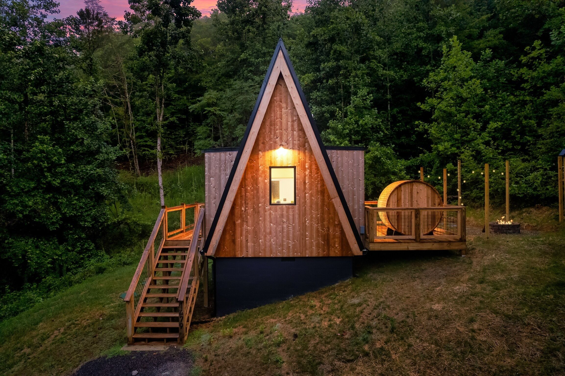 A wooden cabin with a triangular roof, a staircase leading to a deck, and a barrel structure nearby.
