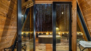 Una cabaña moderna con un vidrio que da a una terraza de madera, un jacuzzi y un área de estar.