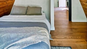 Un dormitorio con techo inclinado, vigas de madera, una cama y un pasillo que conduce a una cocina.