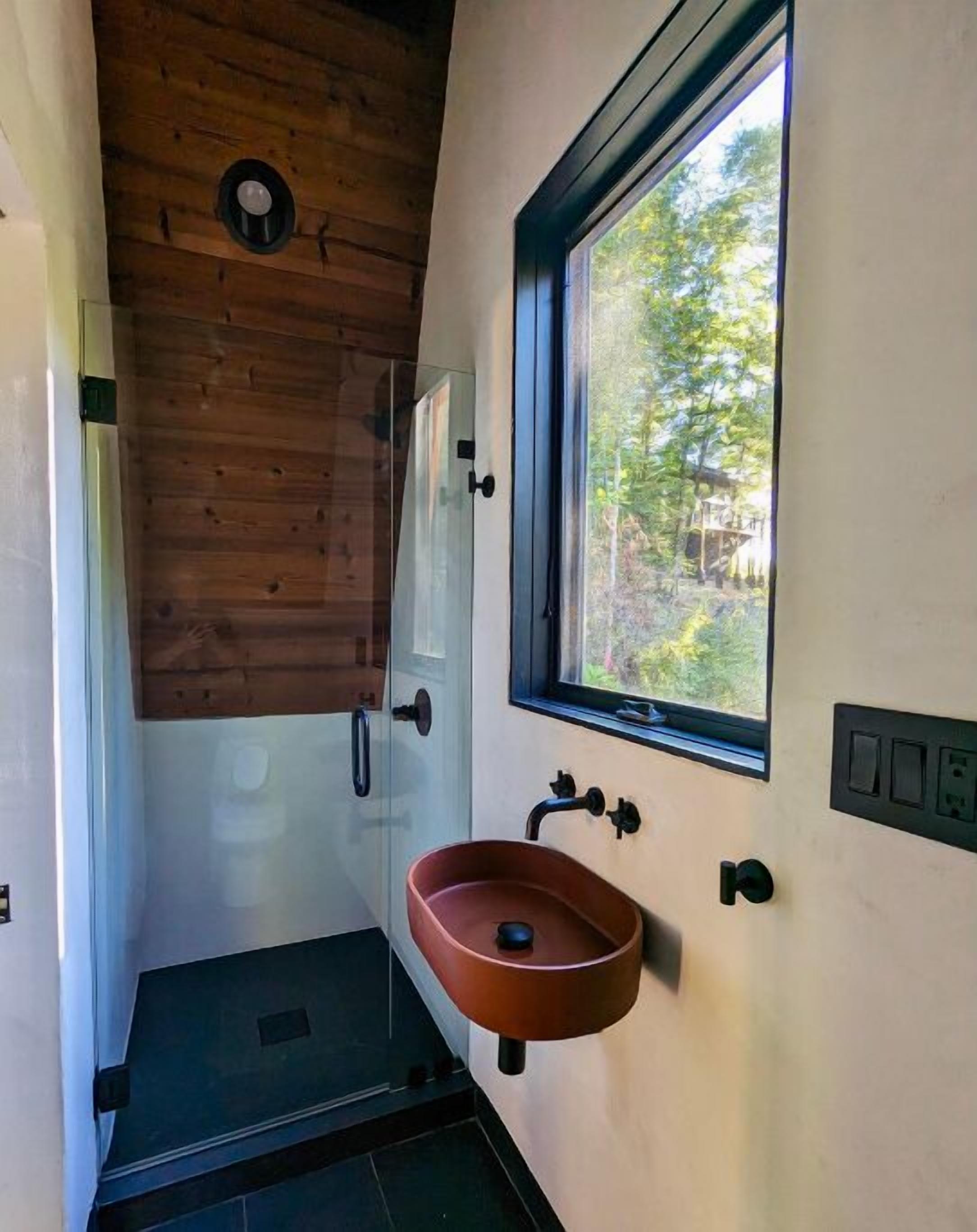 Ein Badezimmer mit Holzboden, einem Fenster, einem Waschbecken und einer Dusche.