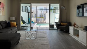 A modern living room with a sofa, a glass coffee table, and a view of a pool and buildings outside. - 3-bedroom house in Orlando close to Disney with Customizable children's room (Clermont)
