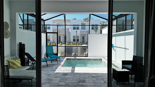 A modern interior with a sliding glass door leading to an outdoor patio area featuring a pool, seating, and a view of neighboring buildings. - 3-bedroom house in Orlando close to Disney with Customizable children's room (Clermont)