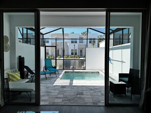 Ein modernes Interieur mit einer Schiebetür, die auf eine Außenpatio mit Pool, Sitzgelegenheiten und Blick auf umliegende Gebäude führt.