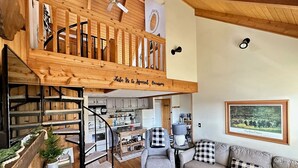 Un vaste espace de vie aménagé dans un style industriel, avec un escalier en bois, un coin salon confortable et une cuisine à l’arrière-plan.