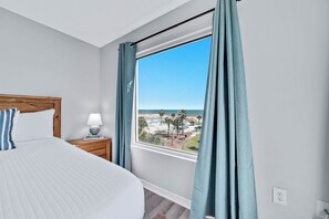 Un dormitorio con una cama grande, una mesita de noche con lámpara y una ventana con cortinas.