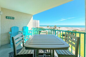Un balcón con una mesa y sillas, un letrero que dice "SURF" y vistas a la playa y al océano.