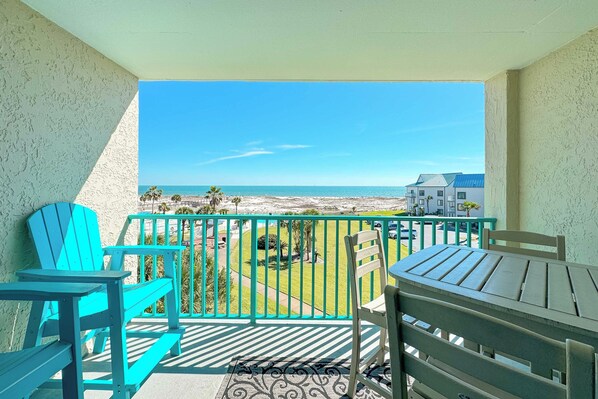 Un balcón con vista a la playa, una mesa, sillas y una barandilla.