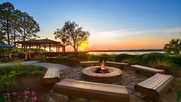 An outdoor seating area with a fire pit, benches, and a gazebo overlooking a body of water during sunset. - arriott Harbour Point 2025 PGA Tour RBC Heritage Week - 2 Bd, 2 Bath Villa (Hilton Head)