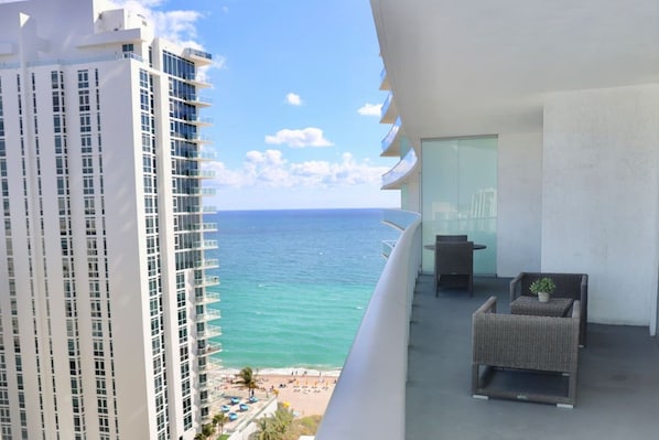 A balcony with a view of the ocean, a high-rise building, and outdoor furniture. - Ocean View Apt on the Beach 2 Bedroom 2 Bath. (Hollywood)