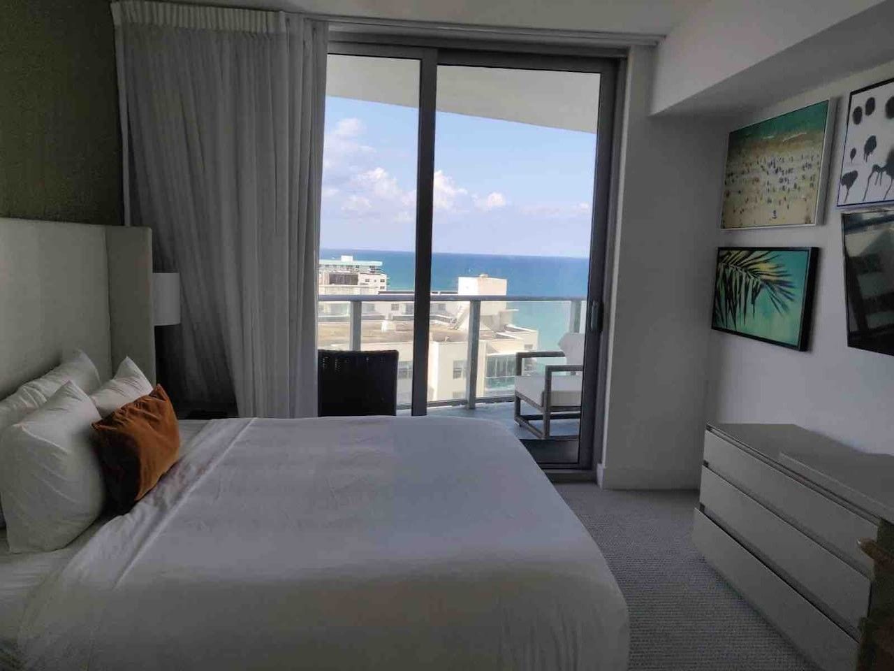 Une chambre d’hôtel avec un grand lit, un balcon donnant sur la mer et des œuvres d’art accrochées au mur.