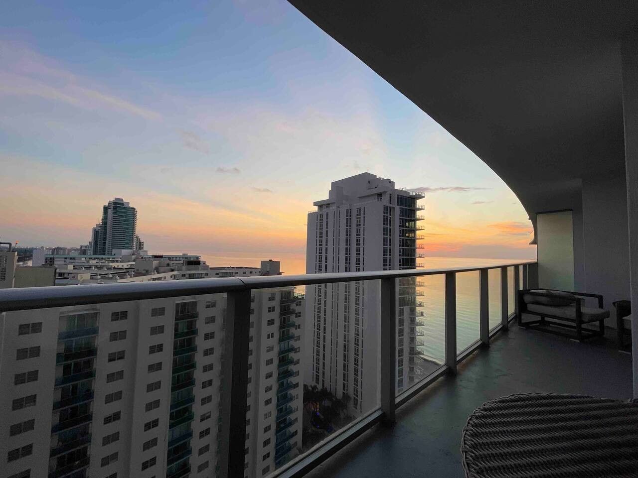 Un balcon offrant une vue sur les gratte-ciel d’une ville et sur une étendue d’eau au coucher du soleil.