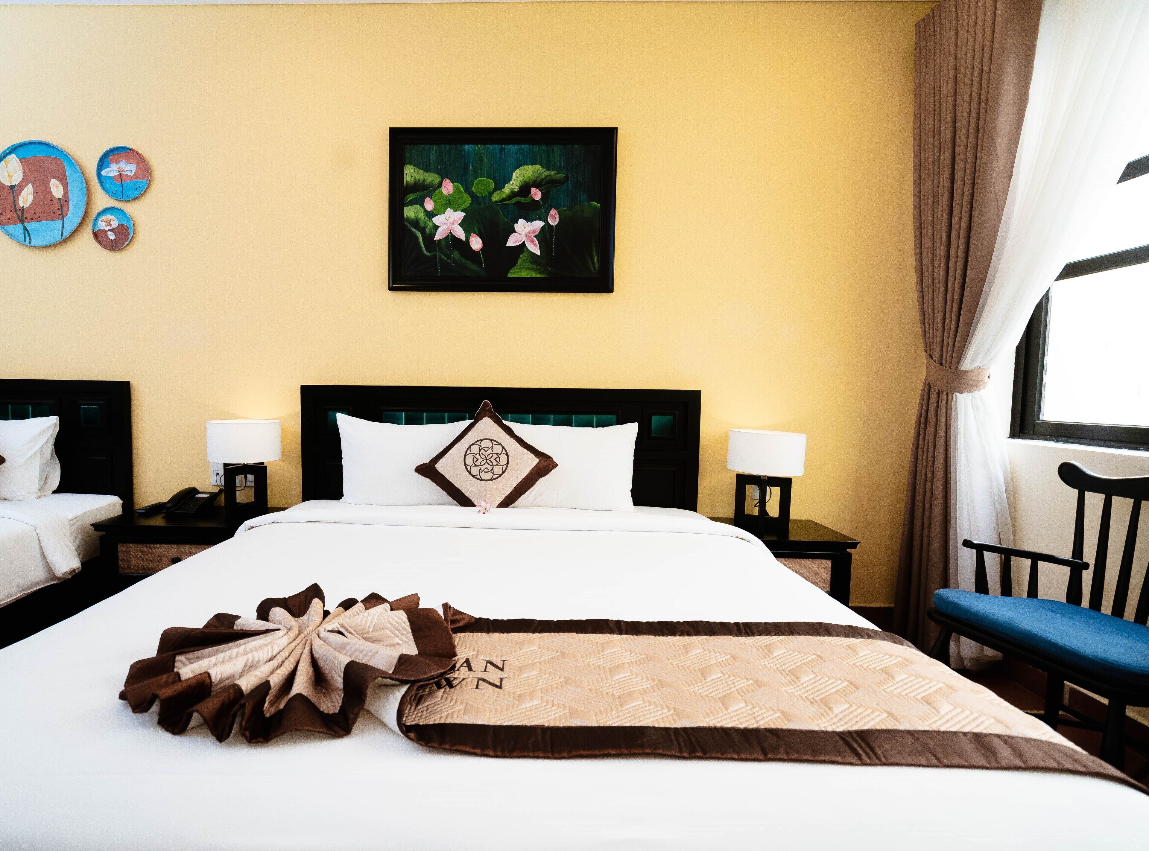 Habitación de hotel con una cama grande, dos mesitas de noche, una silla y un ventanal con cortinas.