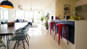 Cozinha moderna com ilha central, banquetas vermelhas e sala de jantar com cadeiras de vidro.