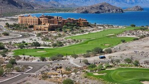 A resort with a golf course, a large building, and mountains in the background.