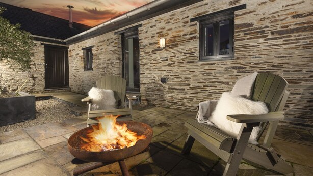 A stone building with a fire pit and two Adirondack chairs.