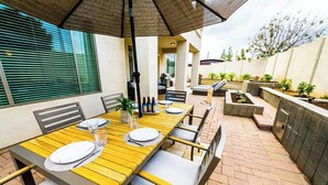 An outdoor patio with a wooden table set for dining, surrounded by chairs and an umbrella. - Pueblo Viejo (Scottsdale)