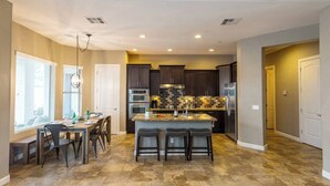 A spacious kitchen with dark cabinets, a central island with bar stools, and a dining area with a table and chairs. - Pueblo Viejo (Scottsdale)