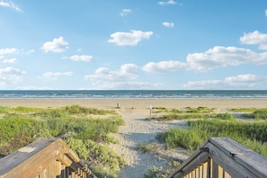 A beach view with a wooden boardwalk leading to the shore, sandy beach, and grassy dunes.