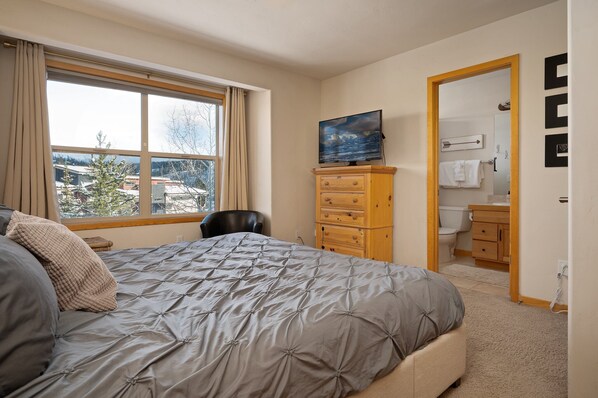 Un dormitorio con una cama grande, un aparador, un televisor y vistas al exterior.