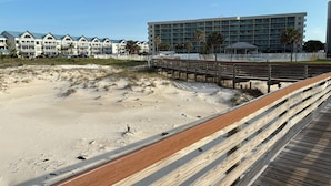 A beach with a wooden boardwalk leading to a building with multiple balconies. - Welcome to SEA-Nanigans. Unit #1366. 
A charming condo with Gulf Views. (Gulf Shores)