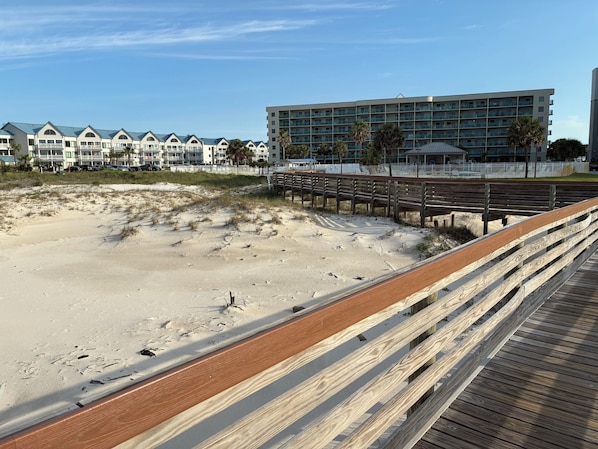 Ein Strand mit einer Holzpromenade, die zu einem Gebäude mit mehreren Balkonen führt.