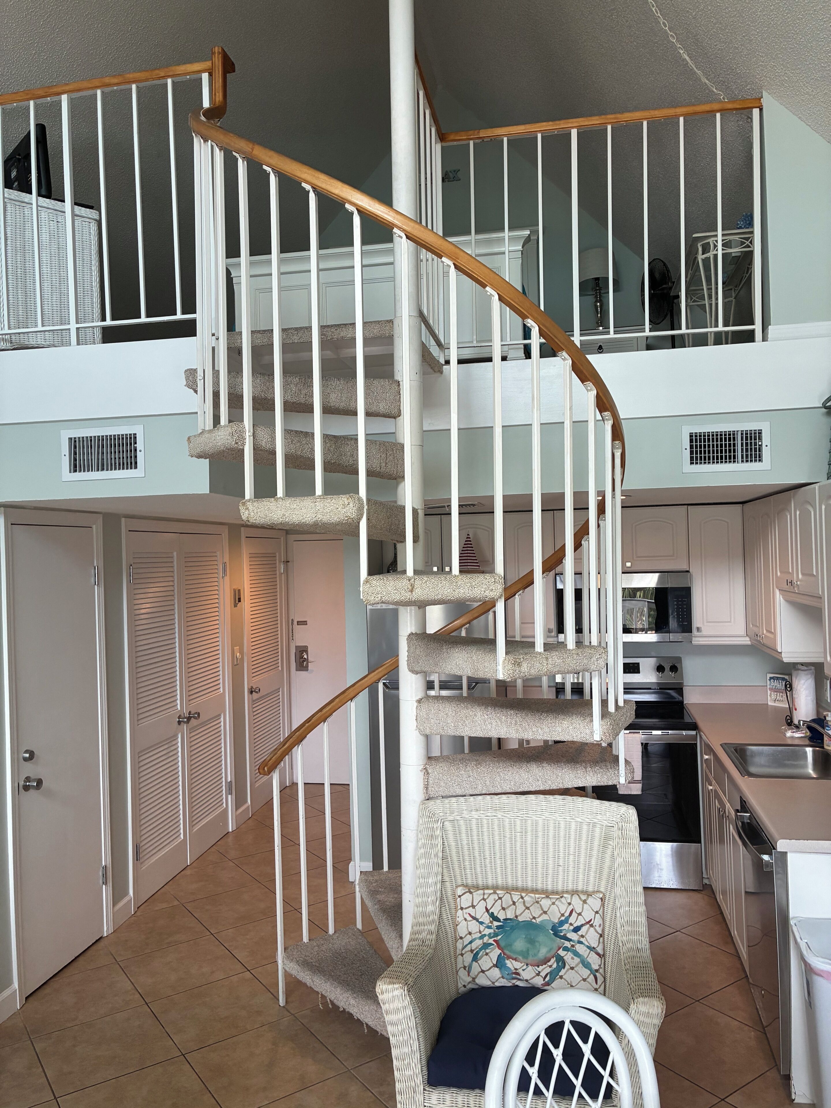 A two-story home with a wooden spiral staircase, a kitchen with modern appliances, and a wicker chair with a decorative pillow.