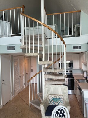 Ein zweistöckiges Haus mit einer Holzspirale, einer Küche mit modernen Geräten und einem Korbstuhl mit Zierkissen.