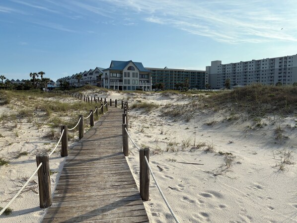 Une promenade en bois mène à un hôtel en bord de mer, doté de nombreux balcons et d’un design moderne.