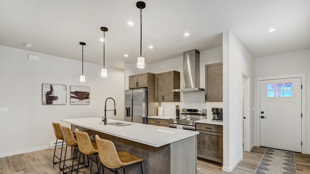 A modern kitchen with a central island, bar stools, stainless steel appliances, and pendant lighting. - El Paso Executive Suites | Pet Friendly NEW BUILD (Colorado Springs)