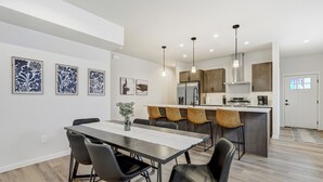 A modern kitchen with a central island, pendant lighting, and a dining area with a table and chairs. - El Paso Executive Suites | Pet Friendly NEW BUILD (Colorado Springs)