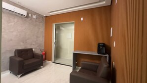 A modern hotel room with a wooden panel wall, a glass door leading to a shower area, two dark sofas, a small table with a radio, and a fire extinguisher. - Pousada Princesa do Sertão (Piranhas)