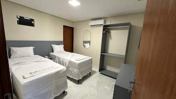 A hotel room with two beds, a wardrobe, a mirror, and an air conditioning unit.