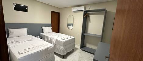 Habitación de hotel con dos camas, un armario, un espejo y un equipo de aire acondicionado.