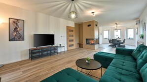 Una sala moderna con un televisor de pantalla plana grande, sofás verdes, una chimenea y un comedor con mesa y sillas.