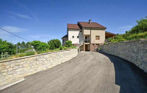 A two-story house with a stone wall on one side and a paved driveway leading to the entrance.