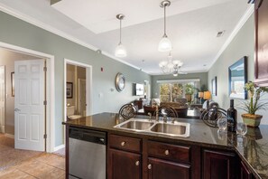 A kitchen with a double sink, dark wooden cabinets, a dishwasher, and a dining area with chairs and a table.