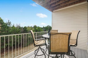 Eine Terrasse mit Tisch und Stühlen, umgeben von einem weißen Geländer, mit Blick auf ein bewaldetes Gebiet.