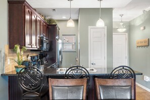 A kitchen with dark wooden cabinets, a granite countertop, and a central island with a sink and seating. - Wooded View 2-Bedroom Condo with Deck, Free Tickets & Close to State Park Marina (Branson)