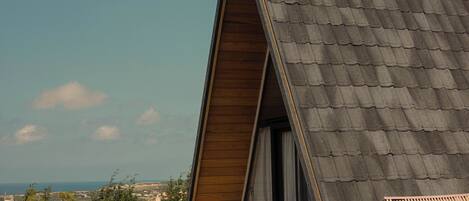 A modern house with a sloped roof, a patio with a bench, and a view of the landscape.