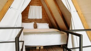 Een gezellige slaapkamer onder de dakrand, met een houten plafond, een bed met witte beddengoed en een hemelbed.