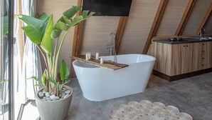 Een moderne badkamer met een vrijstaand bad, een potplant en een groot geweven vloerkleed.