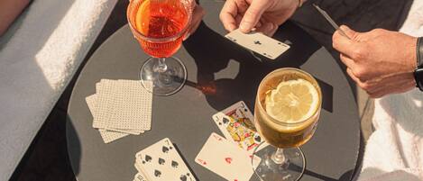 A round table with two drinks, playing cards, and a person holding a playing card.